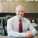 Dr. Andrew Kirsch sitting at desk with arms crossed on desktop, smiling