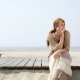 Woman looking off in distance sitting on wooden pier on sandy beach