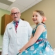 Dr. Scherz standing next to pediatric patient seated on medical table, smiling