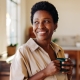 Woman smiling while looking outside window holding coffee with both hands