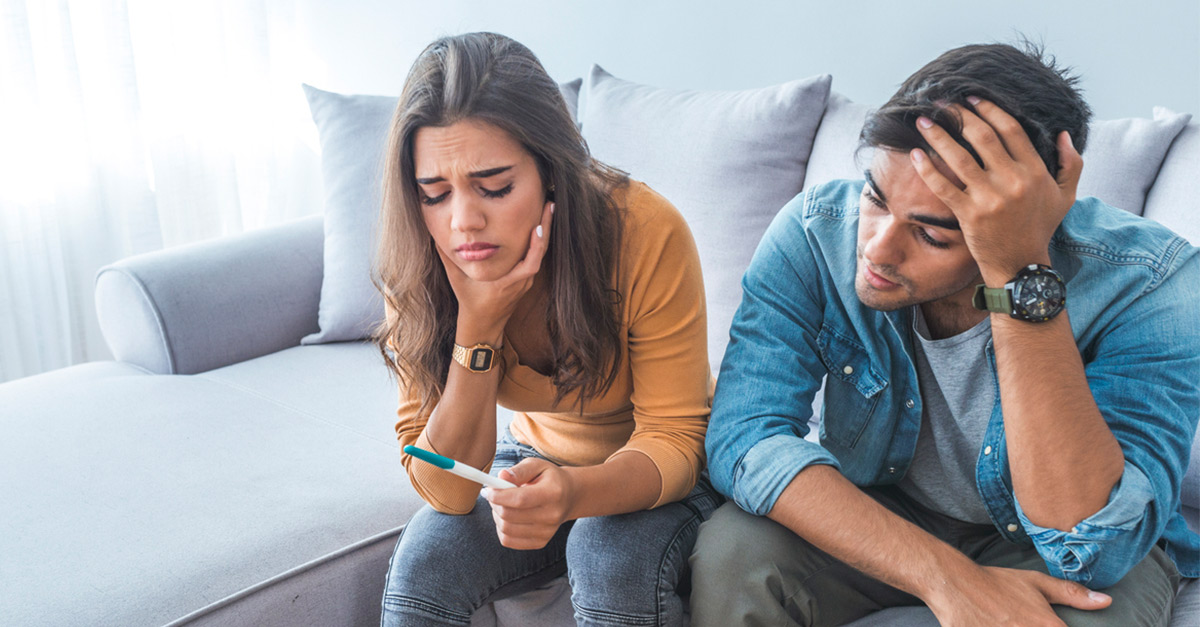 An upset couple looking at a negative pregnancy test due to infertility issues.
