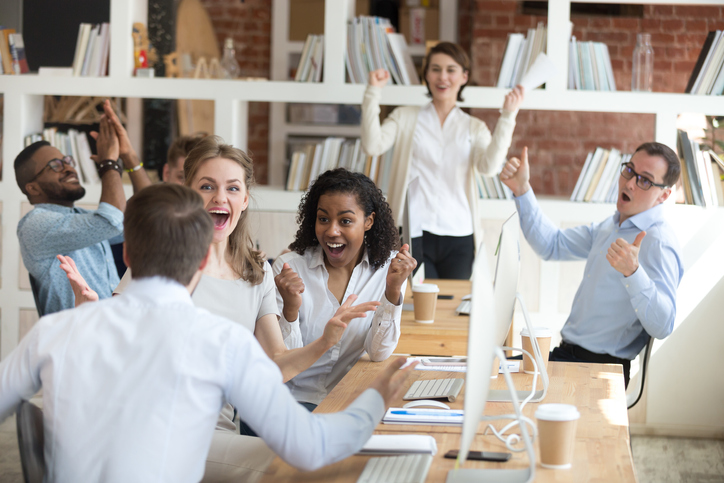 Male worker share good news with multiracial colleagues in shared workplace, diverse employees scream with happiness excited with corporate success or goal achievement, team celebrating win.