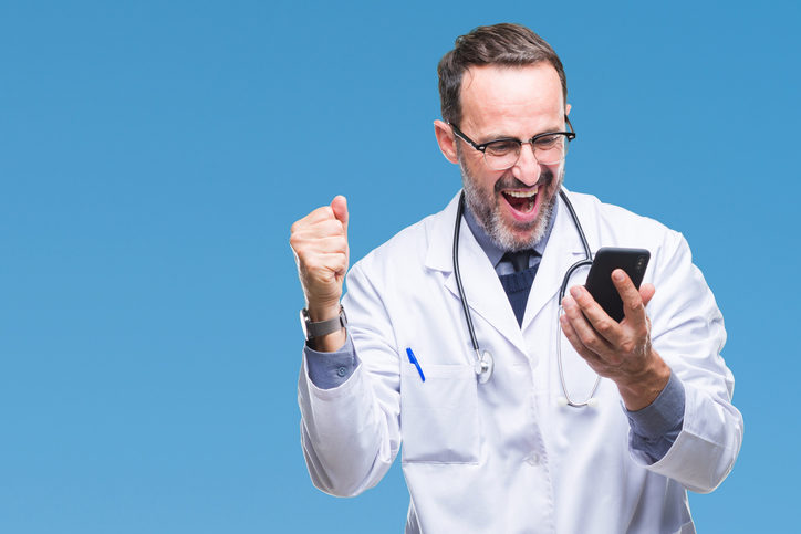 Middle age senior hoary doctor man texting using smartphone over isolated background screaming proud and celebrating victory and success very excited, cheering emotion.