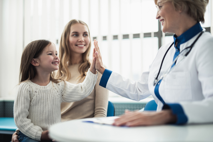 Concept of trustworthy method of consultation in healthcare system. Waist up portrait of smiling little girl giving five to pediatrician lady in medical cabinet, showing the importance of pediatric urology.