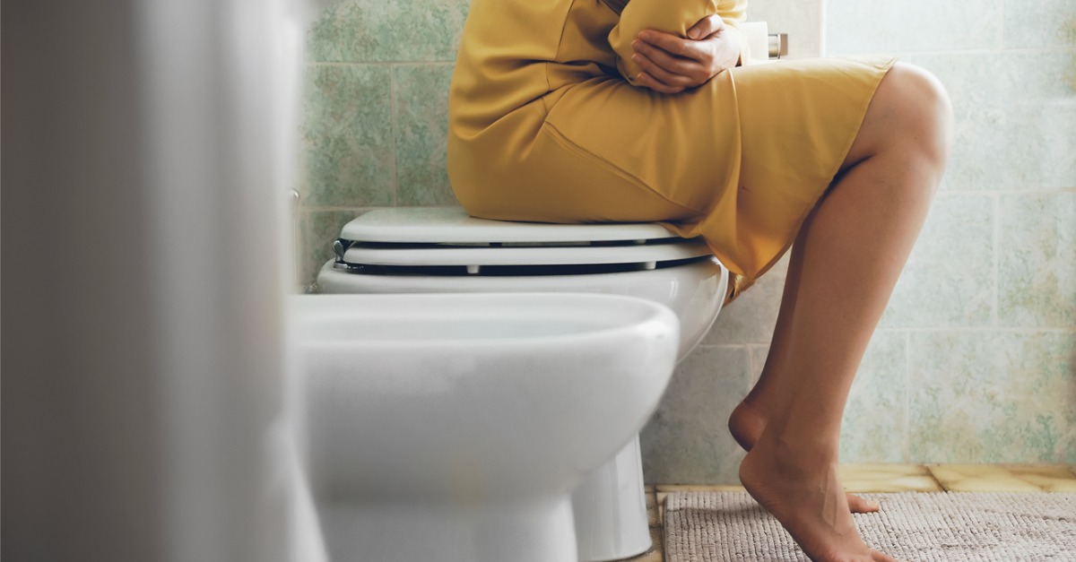 Woman sitting on toilet holding stomach